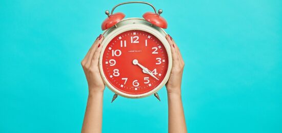 person holding red and beige twin bell analog alarm clock